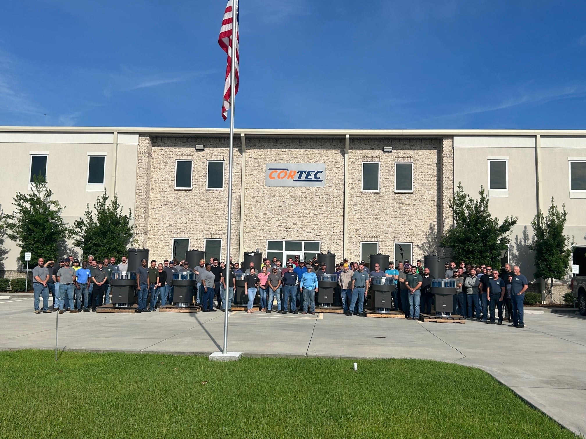 CORTEC employees and product in the front of the building with the American flag.