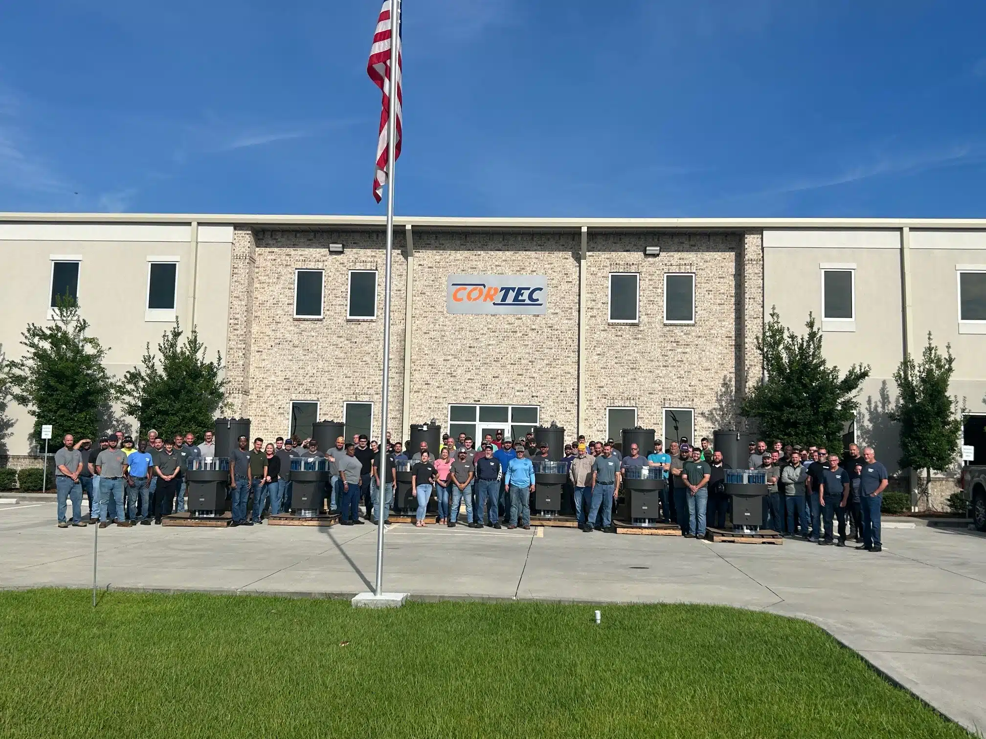 CORTEC employees and product in the front of the building with the American flag.